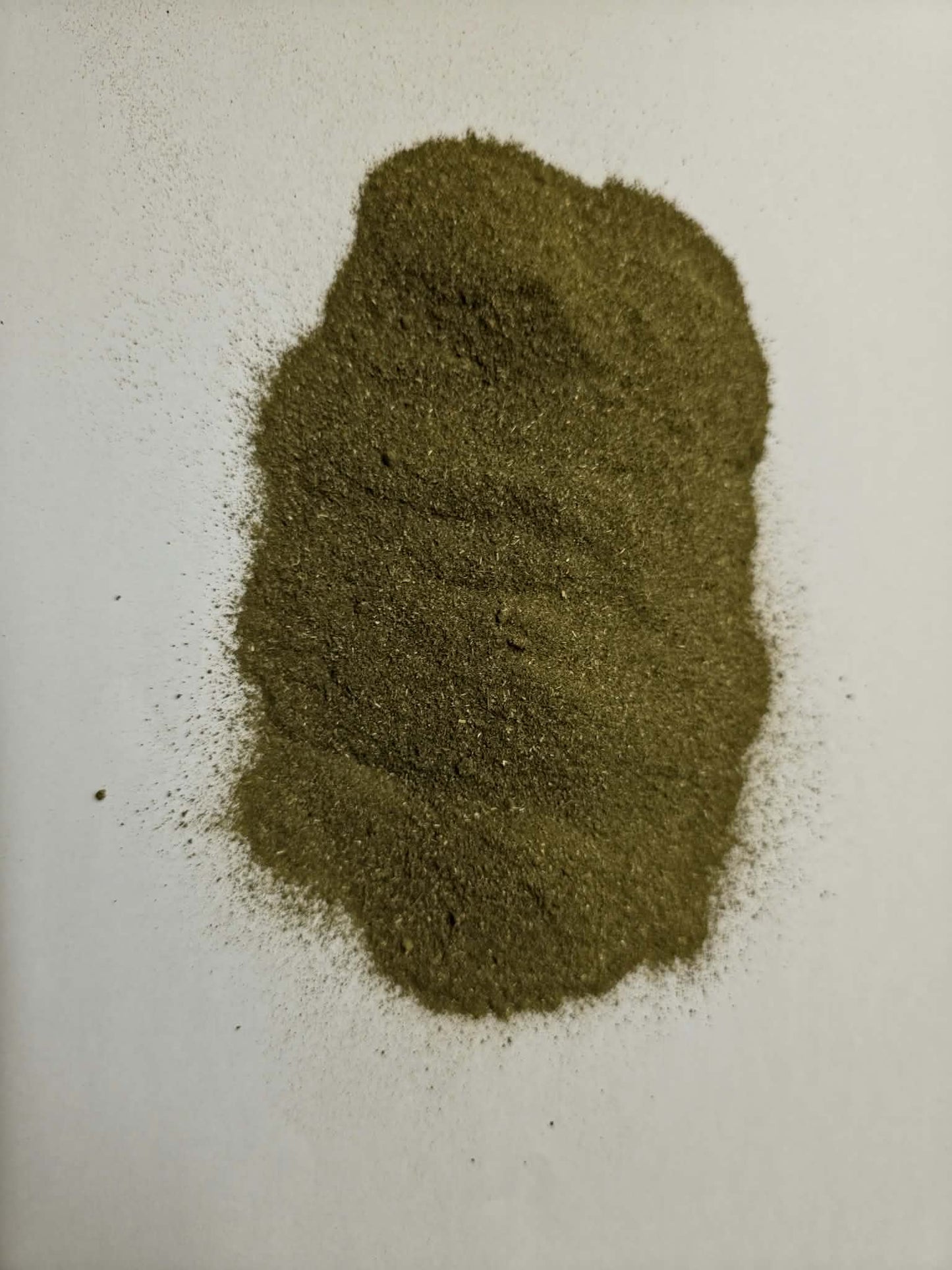 An overhead close-up shot of a mound of loose Apothecary Grade Molokhia Leaf Powder on a white background, highlighting the fine-milled texture and authentic deep olive-green color of pure dried Corchorus olitorius leaves.