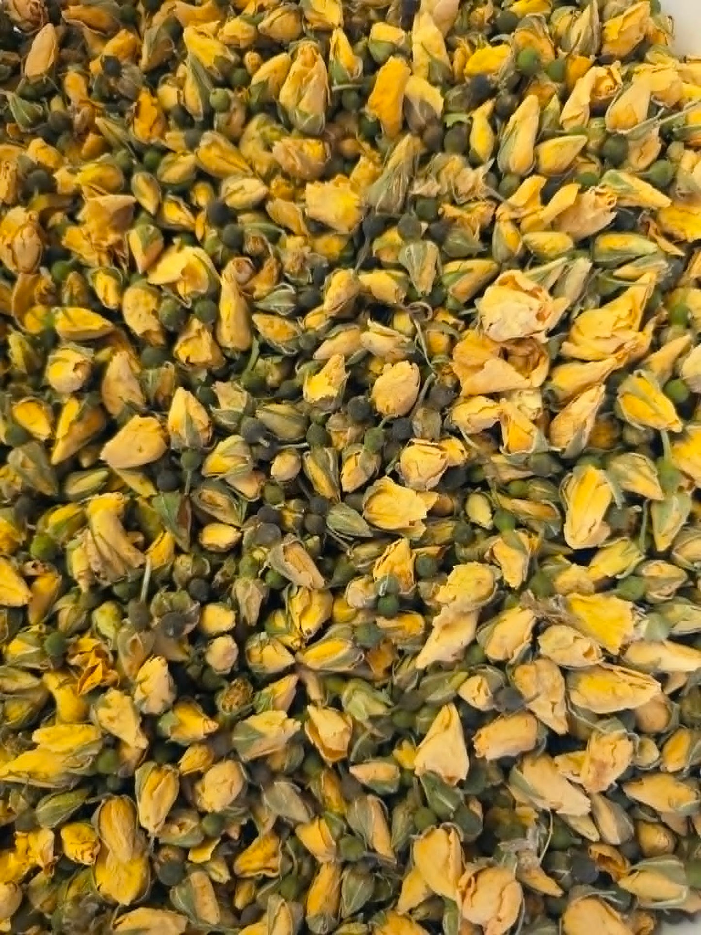 A detailed macro close-up of premium whole dried Yellow Rose Buds (Rosa damascena), showcasing their tightly closed vibrant yellow petals, intact green sepals, and pristine apothecary-grade quality for herbal infusions.