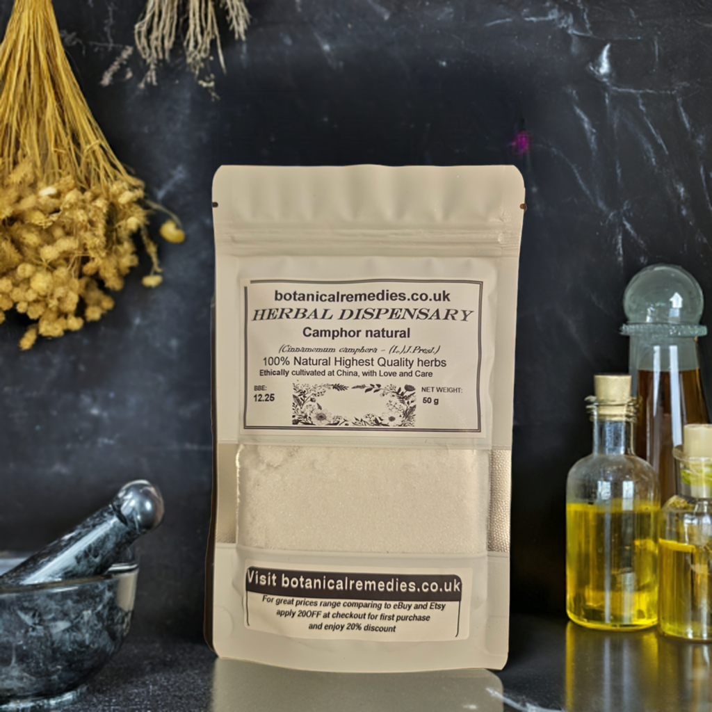 A beige paper bag labeled 'Botanical Remedies Herbal Dispensary Camphor natural' placed on a dark surface with a background of herbs and a glass bottle.