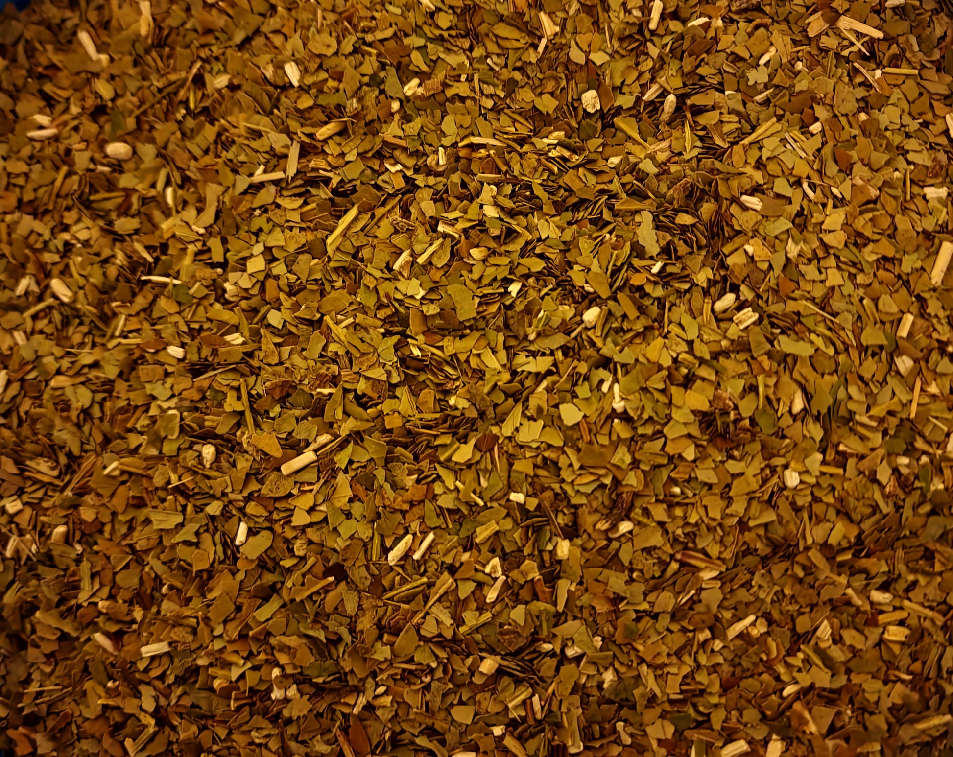 An overhead macro photograph of loose Apothecary Grade Green Yerba Mate, displaying the premium uniform mixture of raw light emerald-green cut leaves and pale cream stem fragments of Brazilian Ilex paraguariensis.