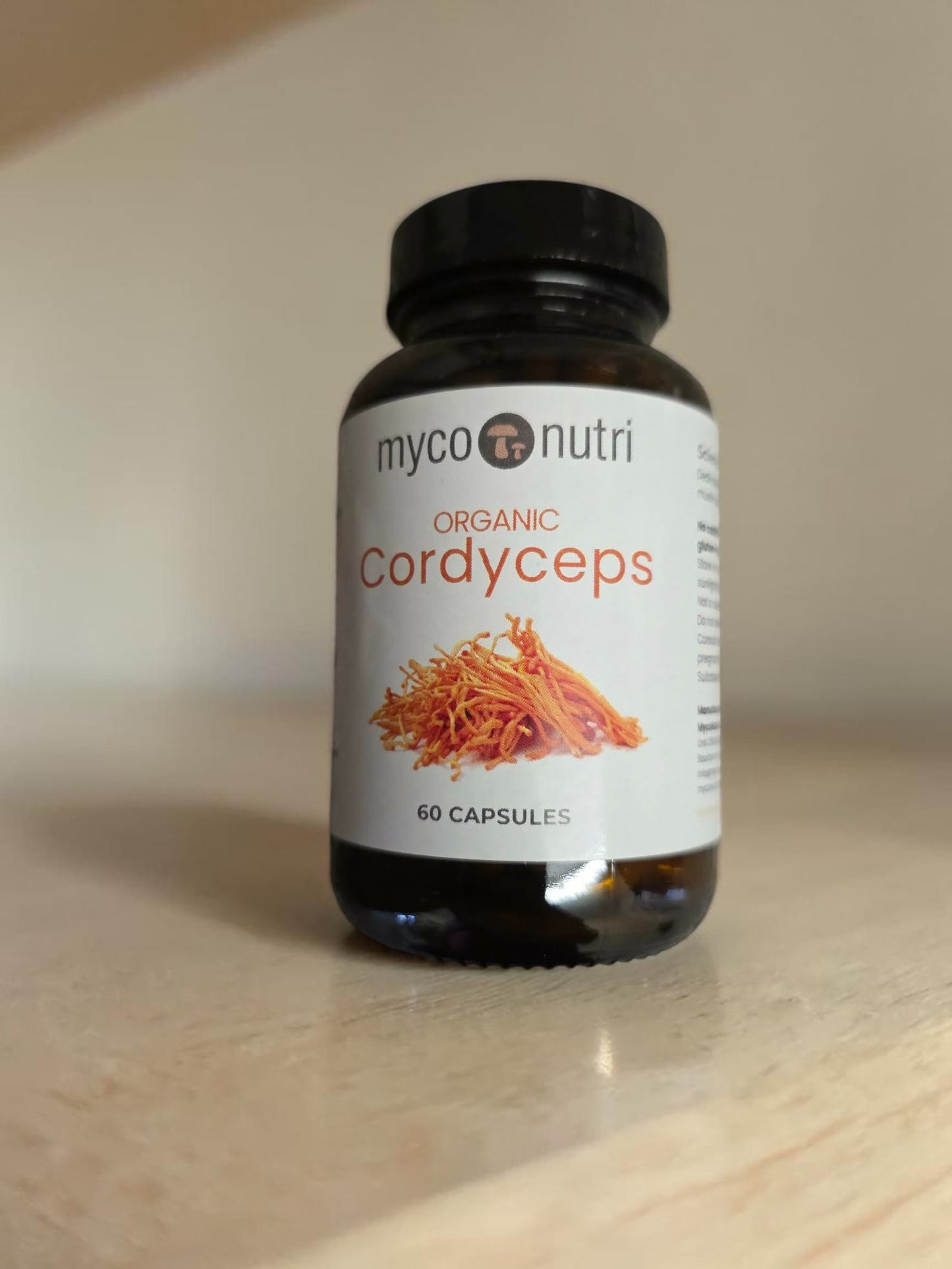 Front view of a premium amber glass apothecary bottle of MycoNutri Organic Cordyceps. The clean white label features a botanical illustration of vibrant orange Cordyceps fruiting bodies and indicates it contains 60 capsules formulated for energy, stamina, and respiratory support