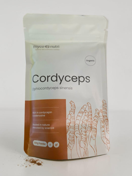 Front view of the clean white and orange stand-up pouch of MycoNutri Organic Cordyceps Powder, 100g. The label highlights that the vegan formulation is rich in cordycepin and adenosine, featuring a botanical illustration of Cordyceps alongside a small dusting of the pure extract powder