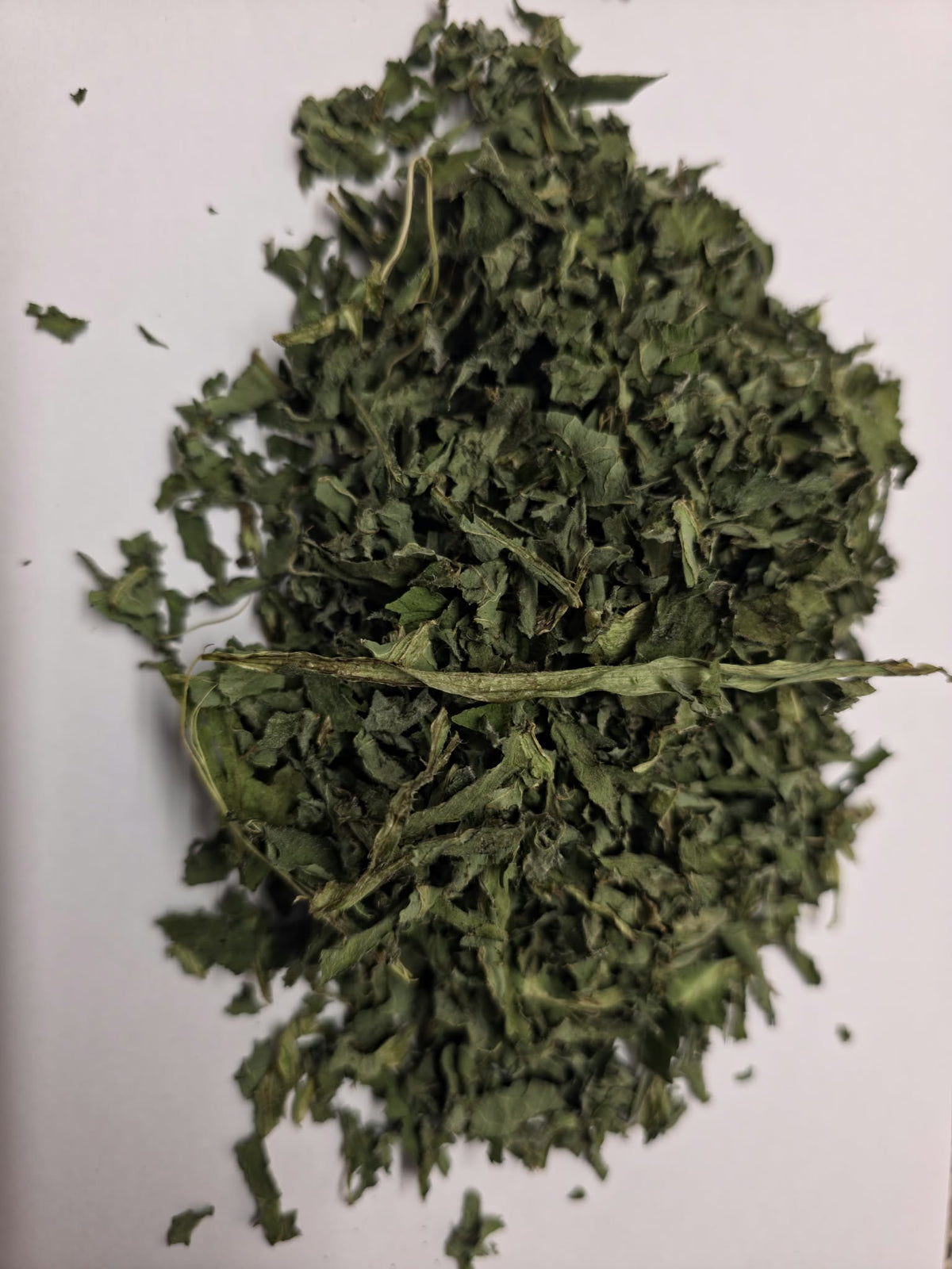 Dried organic and biodynamic comfrey leaf (Symphytum spp) cut pieces showing dark green curled leaves on a plain white background. Ideal for poultices and compresses.