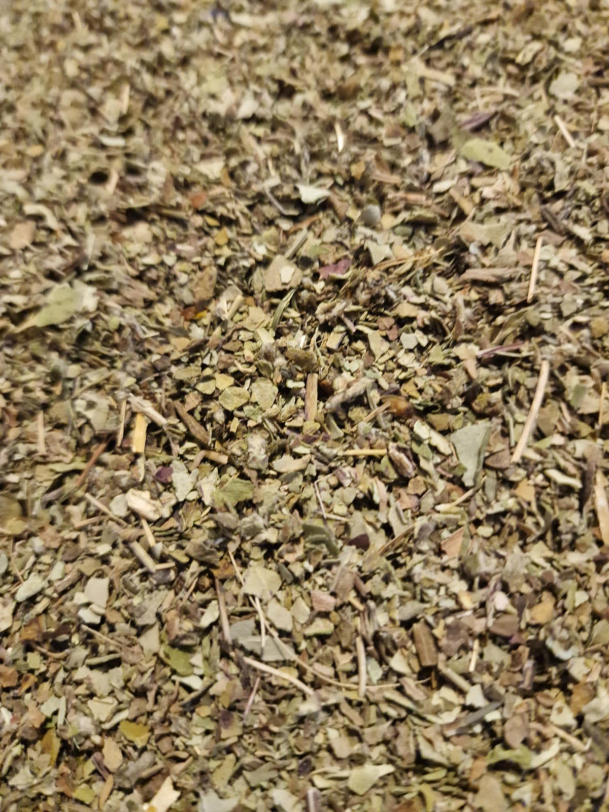 An overhead macro photograph of loose Apothecary Grade dried and cut Organic Coltsfoot Leaf, showing the textured olive-green leaf fragments with their distinctive fuzzy, silver-grey downy backing from wild-grown Albanian Tussilago