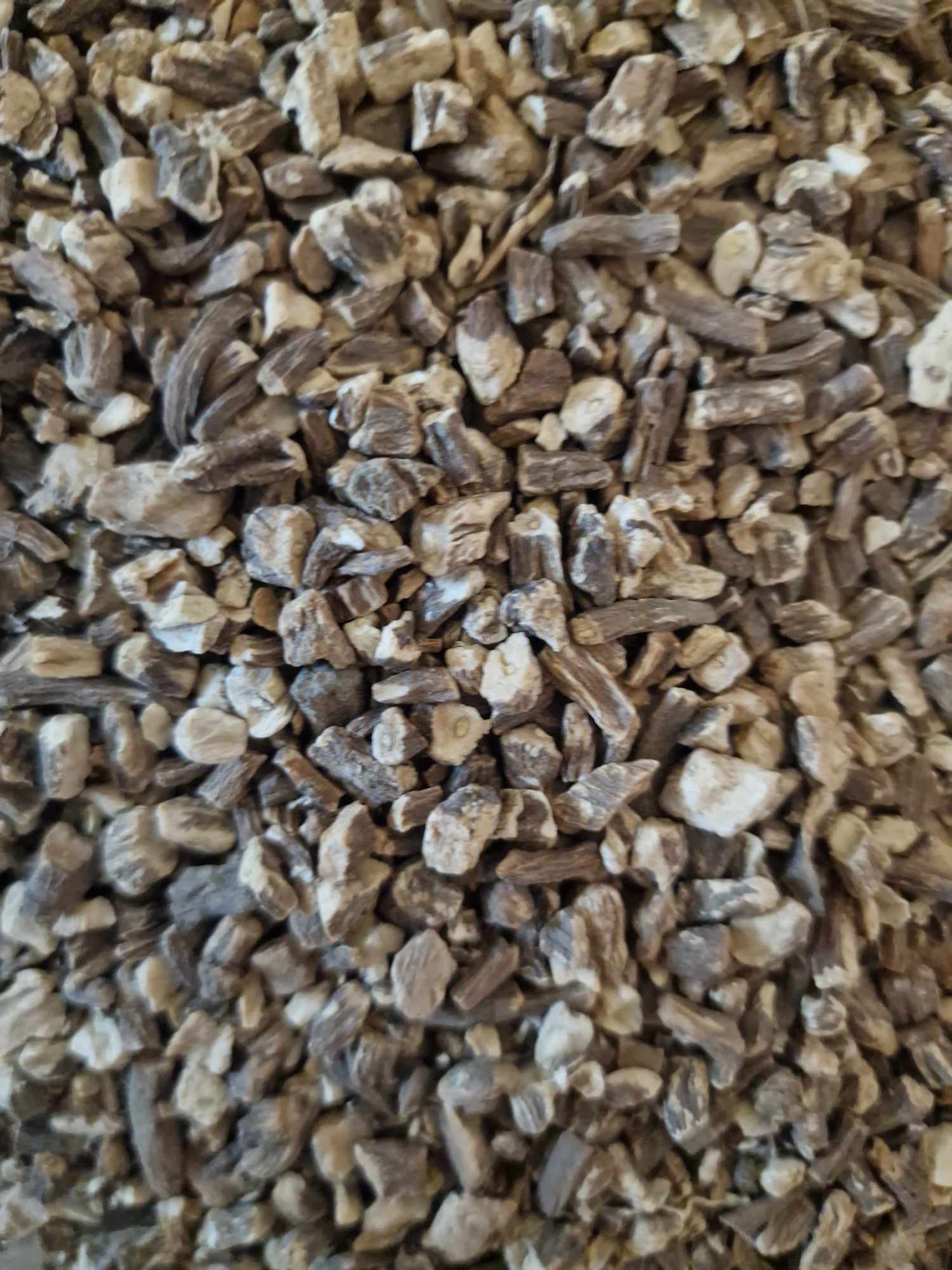 A detailed macro close-up of dried, practitioner-grade Organic Dandelion root pieces (Taraxacum officinale), highlighting the earthy, raw texture of the chopped botanical.