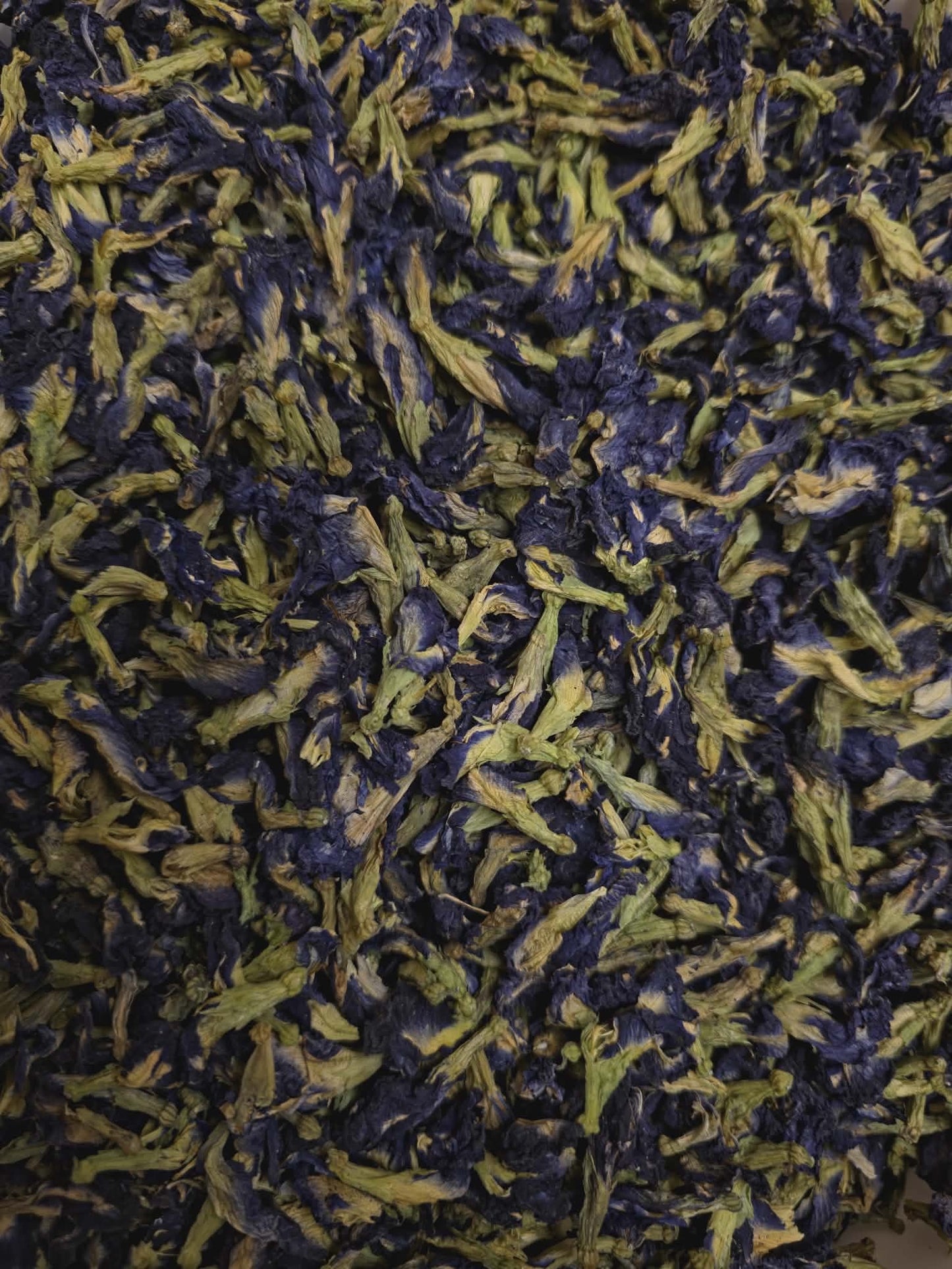 A close-up, highly detailed view of certified organic dried blue Butterfly Pea Flowers (Clitoria ternatea) sourced from Sri Lanka, showcasing their vibrant deep blue petals and pale green intact calyxes
