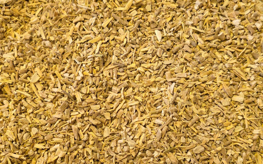 A detailed, close-up texture shot of high-quality, dried, and irregularly cut Ashwagandha root pieces, displaying their natural fibrous texture and light yellow-tan color. This view shows a bulk quantity of the material