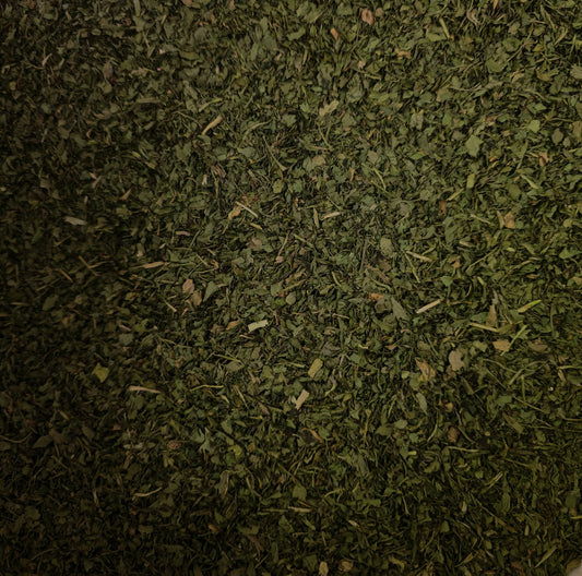A close-up macro photograph of premium, laboratory-tested dried Coriander leaf (Cilantro). The image highlights the vibrant green, finely chopped texture of this 100% pure botanical, expertly cultivated in Italy and perfectly prepared for holistic culinary use and herbal infusions