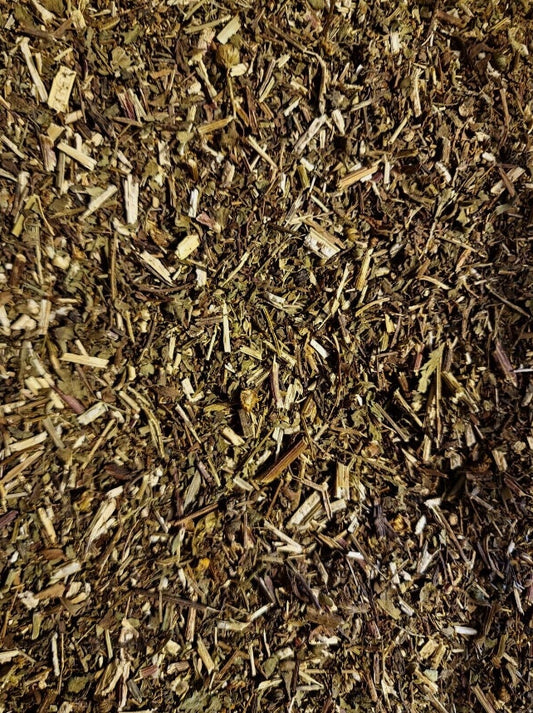 A close-up macro photograph of premium, quality-assured dried Feverfew herb (Tanacetum parthenium). Cultivated and wild-grown in Poland, the image highlights the finely chopped texture of this 100% pure botanical, showcasing a natural mix of green leaves and pale stems prepared for traditional herbal infusions