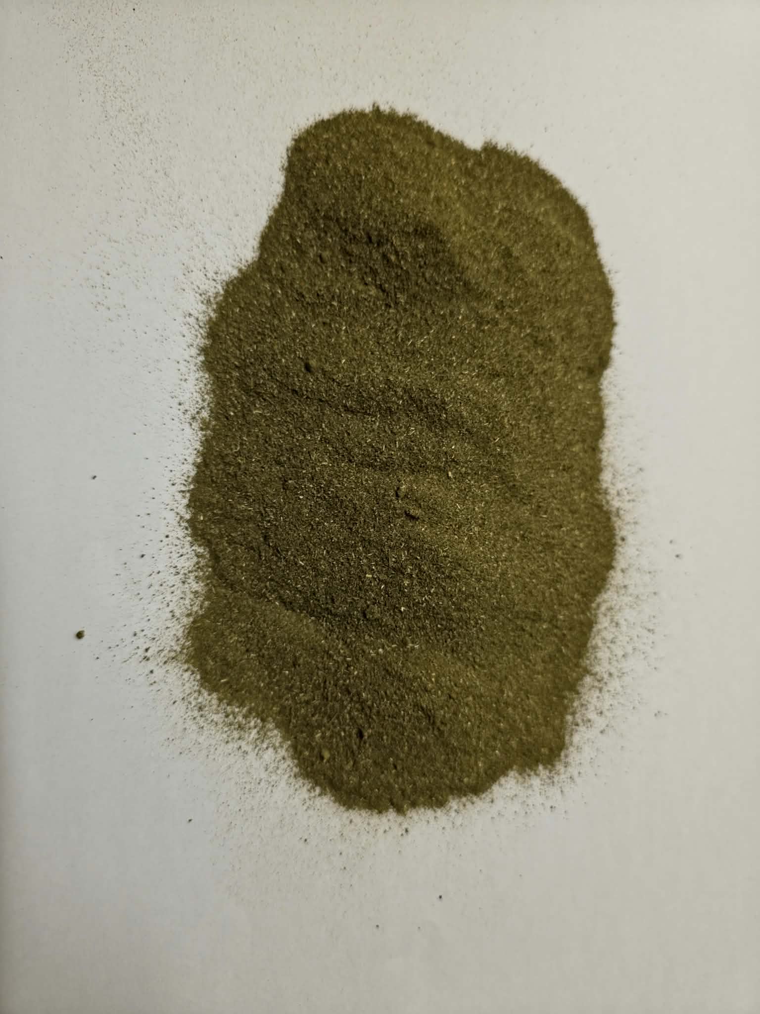 An overhead close-up shot of a mound of loose Apothecary Grade Molokhia Leaf Powder on a white background, highlighting the fine-milled texture and authentic deep olive-green color of pure dried Corchorus olitorius leaves.