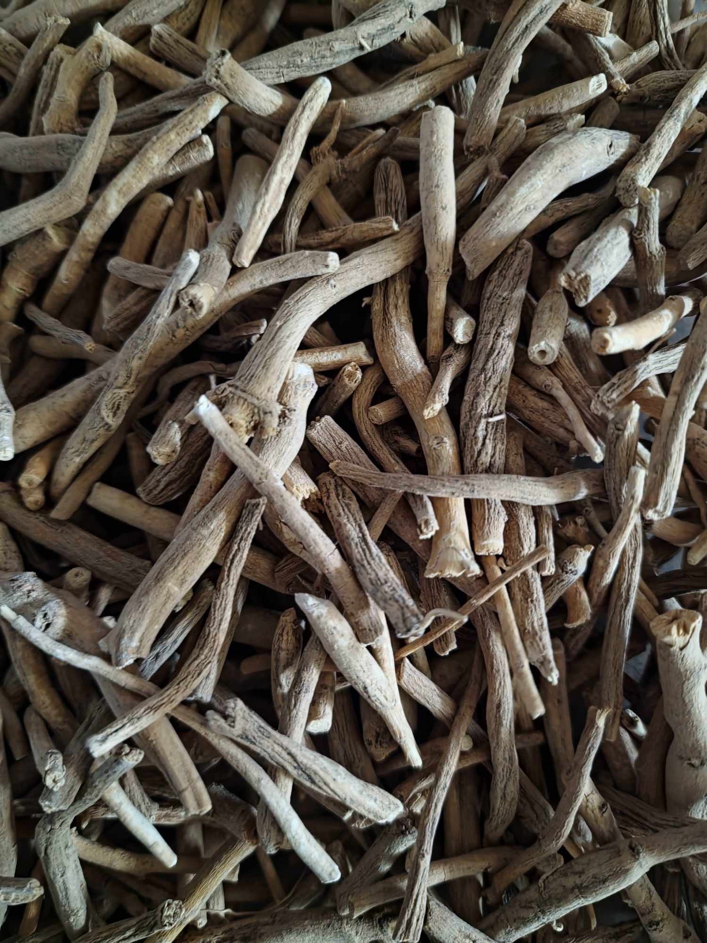 A detailed close-up view of dried, premium organic Ashwagandha root large pieces, showing the natural woody texture of the raw botanical.