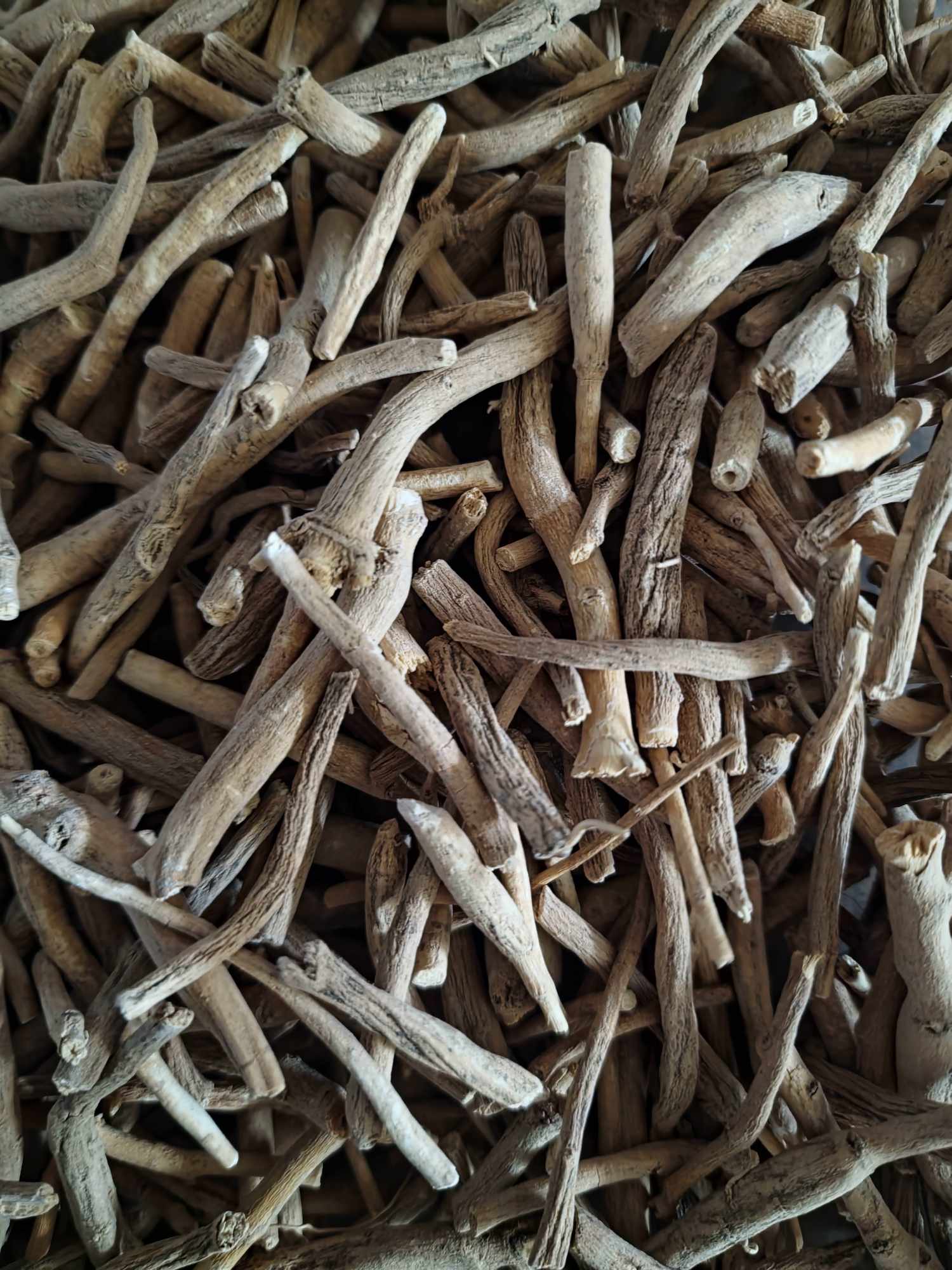 A detailed close-up view of dried, premium organic Ashwagandha root large pieces, showing the natural woody texture of the raw botanical.