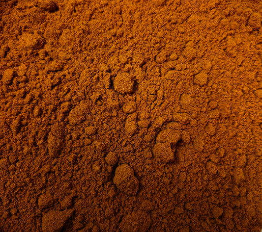 A macro, top-down photograph showing the rich, deep crimson-orange color and naturally clumpy texture of finely milled premium sweet paprika powder