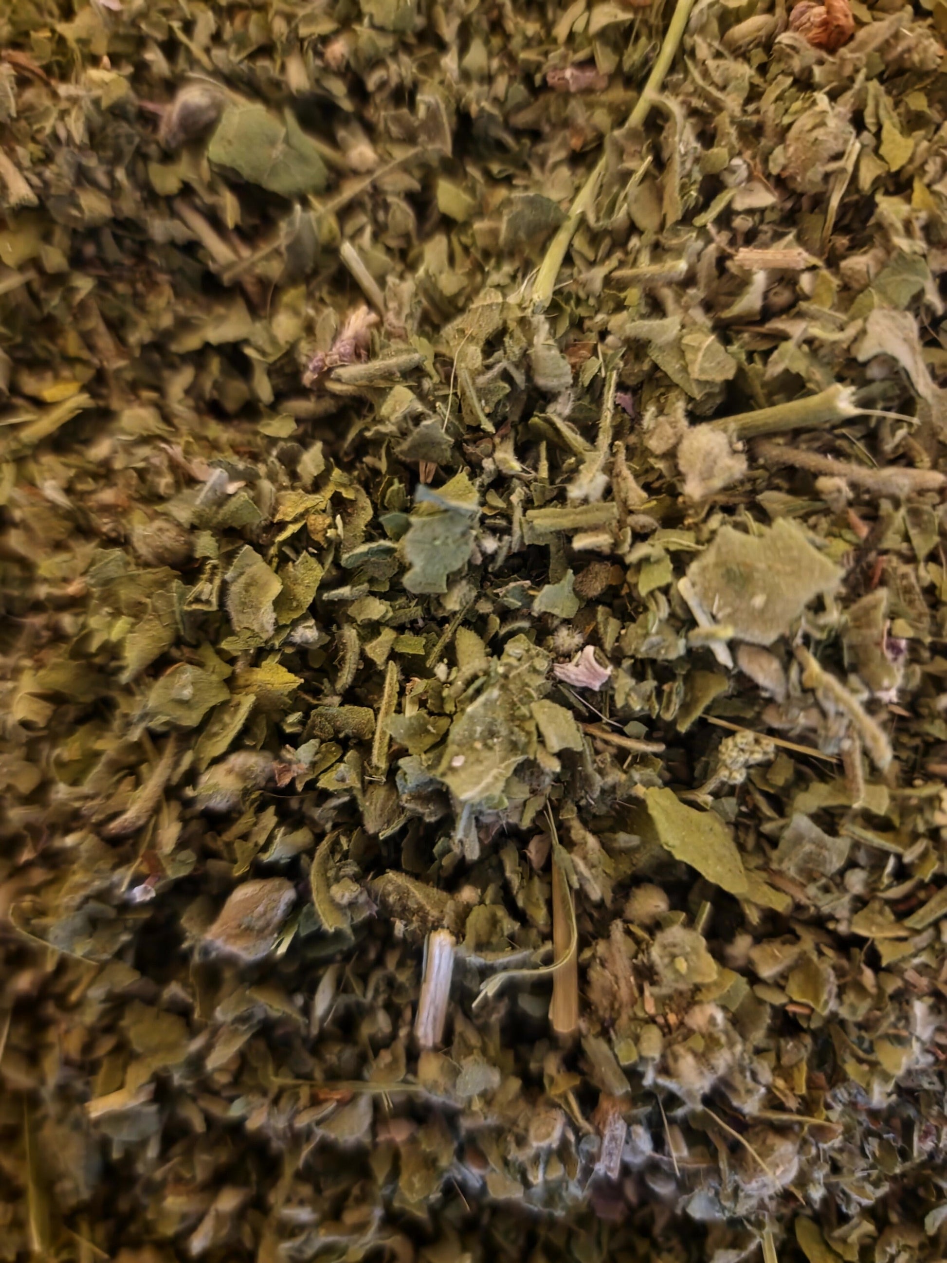 An overhead macro photograph of loose Apothecary Grade dried and cut Marshmallow leaves, showcasing the velvety khaki-green texture and clean cut of wild-grown Polish Althaea officinalis.